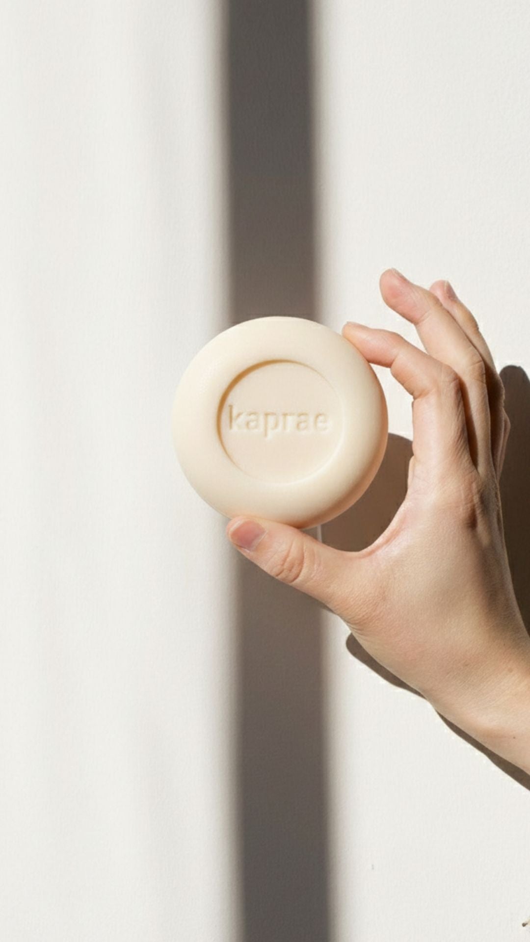 Savon au lait de chèvre Kaprae tenu dans la main, savon naturel pour peaux sensibles, logo Kaprae embossé.
