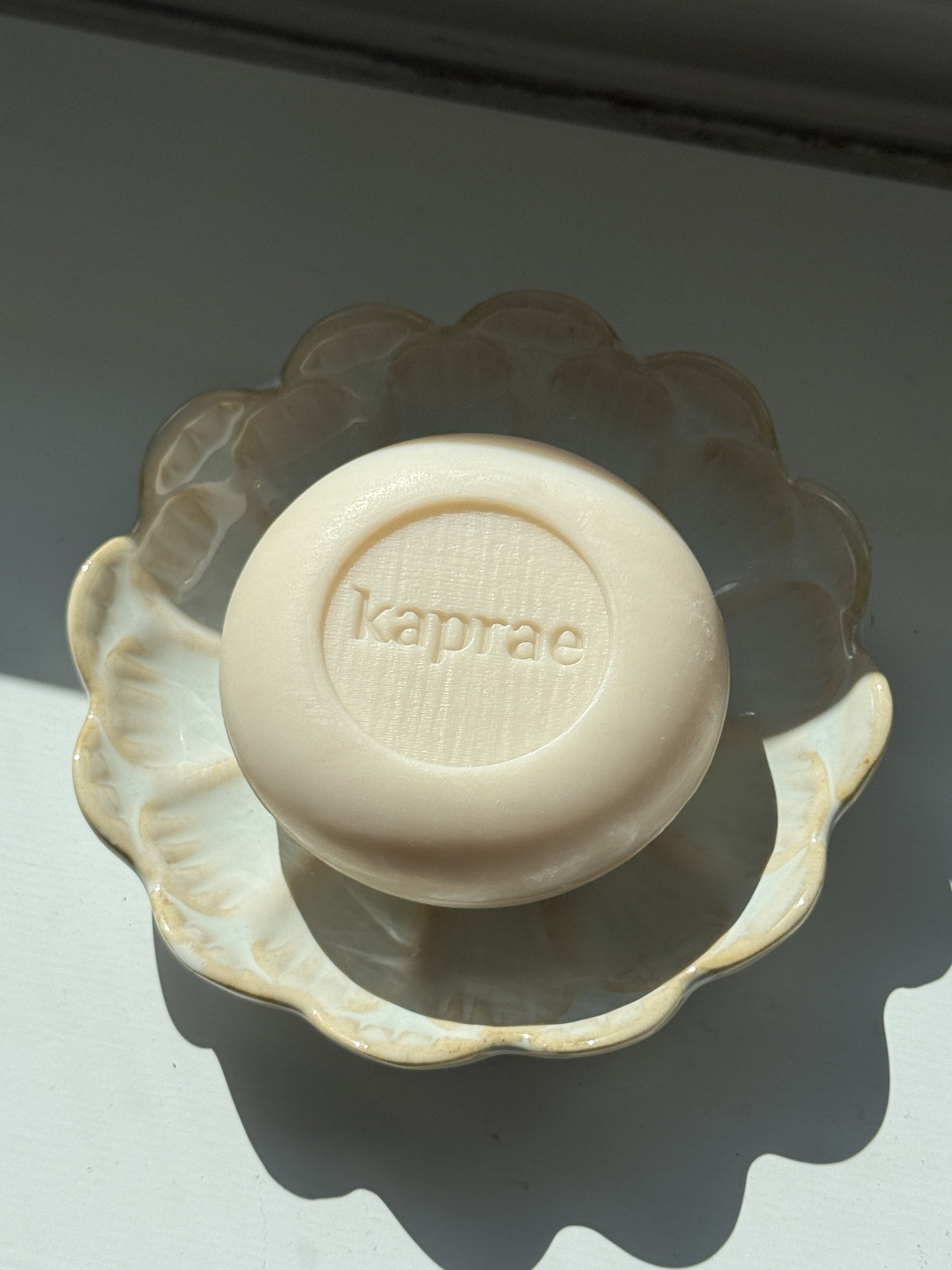 Savon Kaprae au lait de chèvre posé dans une coupelle en céramique, éclairé par une lumière naturelle douce.