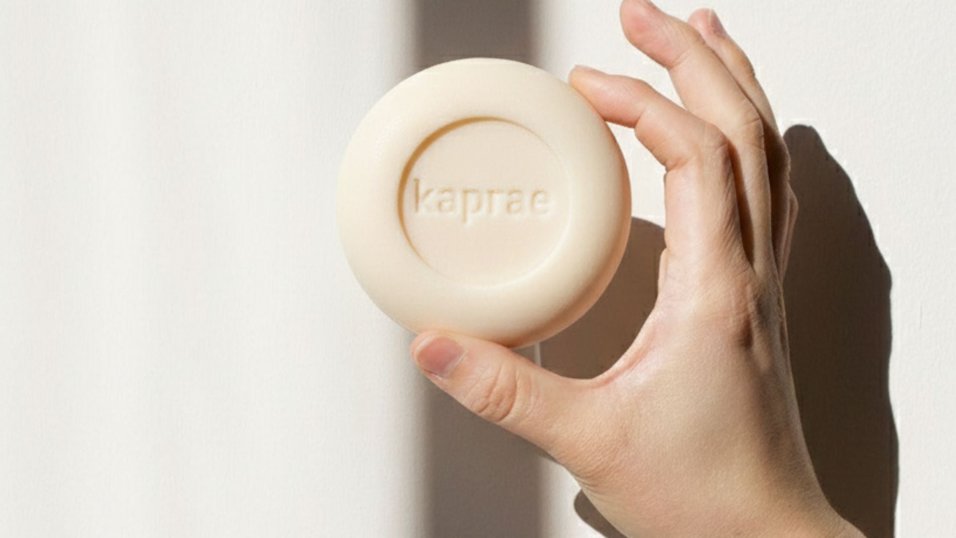 Savon au lait de chèvre Kaprae tenu dans la main, savon naturel pour peaux sensibles, logo Kaprae embossé.
